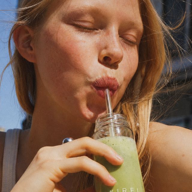 Woman enjoying KIREI iced matcha through a straw in the sunshine